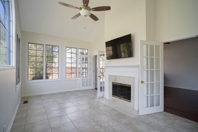 unfurnished living room with a fireplace with flush hearth, a ceiling fan, a wealth of natural light, and high vaulted ceiling