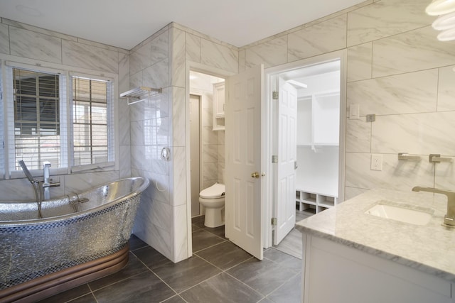 bathroom with a freestanding tub, toilet, tile walls, and vanity