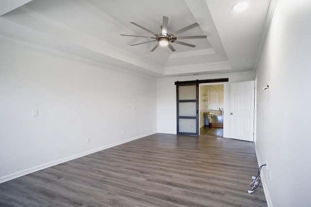 unfurnished bedroom featuring ornamental molding, dark wood-style floors, a barn door, baseboards, and a raised ceiling