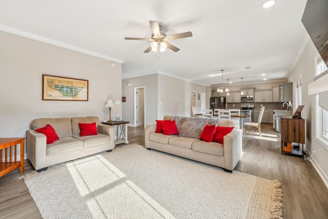 living area featuring wood finished floors, a ceiling fan, baseboards, recessed lighting, and crown molding