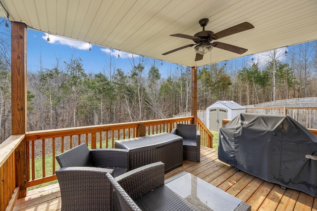 wooden deck featuring grilling area, ceiling fan, fence, an outdoor structure, and a storage unit