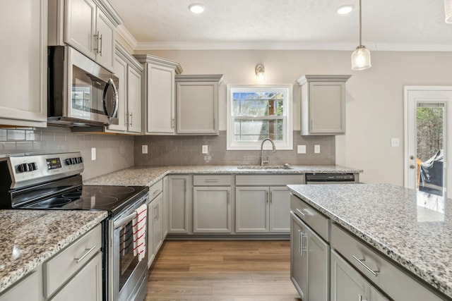 kitchen with a sink, decorative backsplash, ornamental molding, stainless steel appliances, and light wood-type flooring