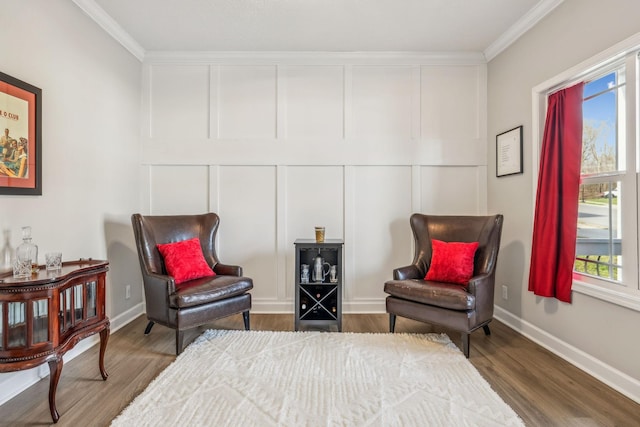 living area with crown molding, a decorative wall, wood finished floors, and baseboards