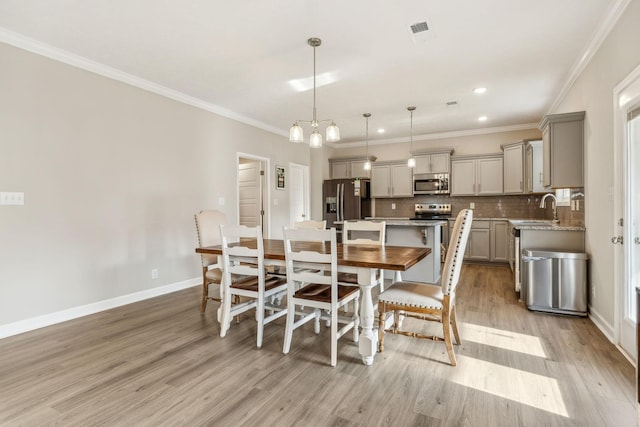 dining room featuring light wood-style flooring, baseboards, and ornamental molding