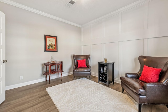 living area featuring visible vents, wood finished floors, crown molding, a decorative wall, and baseboards