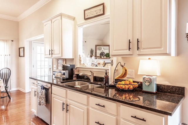 kitchen featuring a sink, stainless steel dishwasher, dark stone counters, light wood-style floors, and crown molding