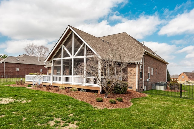 back of house featuring a lawn, fence, roof with shingles, a sunroom, and brick siding