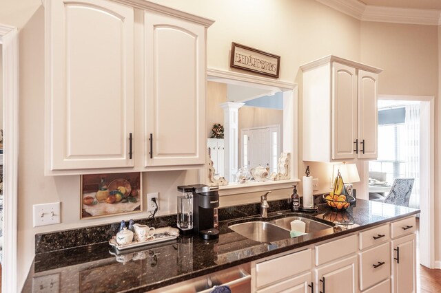 kitchen with ornate columns, dark stone counters, a sink, white cabinetry, and crown molding