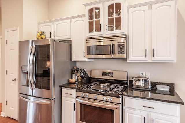 kitchen with dark stone countertops, white cabinets, glass insert cabinets, and stainless steel appliances