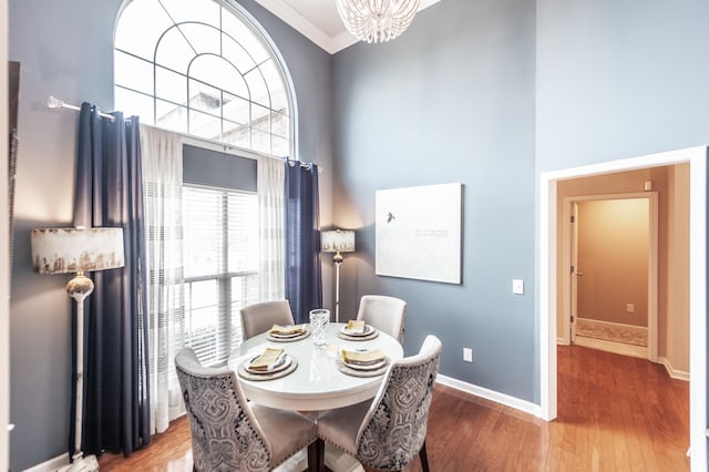 dining area with a notable chandelier, wood finished floors, baseboards, and a towering ceiling