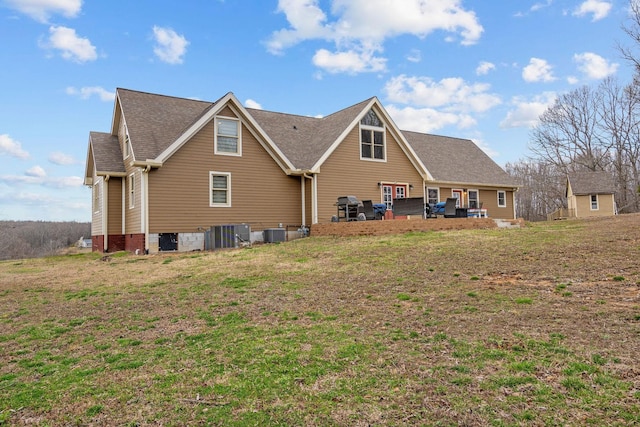 rear view of house with a yard, central AC unit, and roof with shingles
