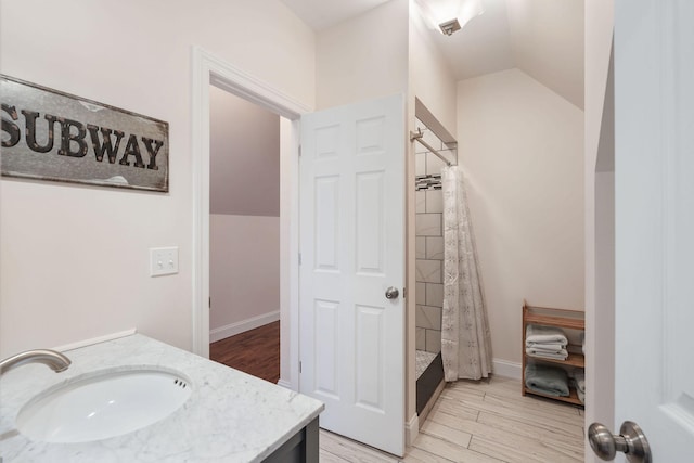 full bath with a tile shower, vanity, lofted ceiling, and wood finished floors