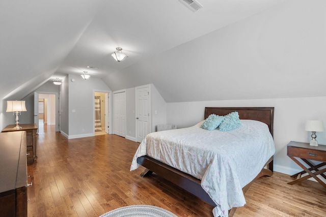 bedroom with vaulted ceiling, visible vents, baseboards, and hardwood / wood-style floors