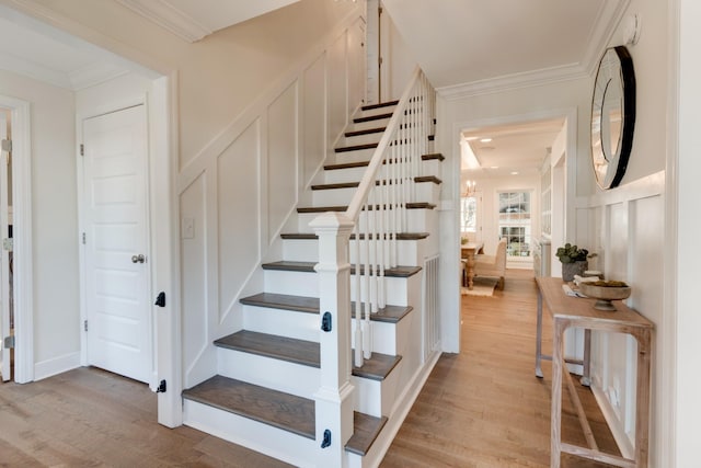 staircase featuring wood finished floors, ornamental molding, and a decorative wall