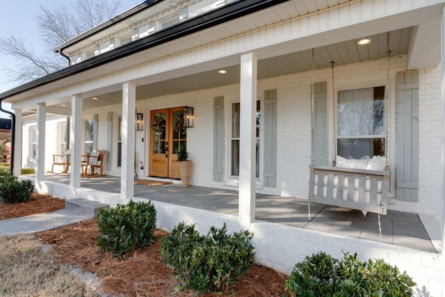 entrance to property with french doors, brick siding, and a porch