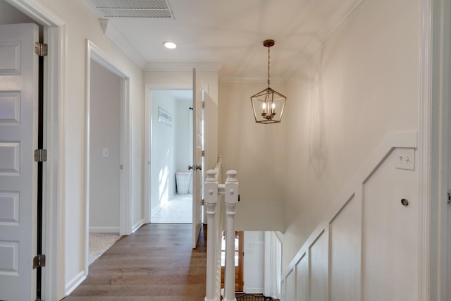 hall with wood finished floors, baseboards, visible vents, and ornamental molding