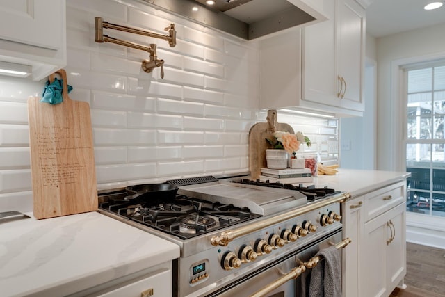 kitchen with light stone countertops, decorative backsplash, wood finished floors, white cabinetry, and high end stainless steel range
