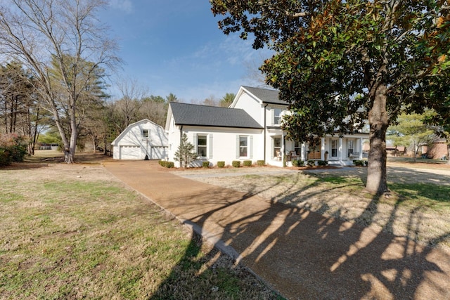 view of front facade with an outbuilding, covered porch, a shingled roof, a front lawn, and a garage