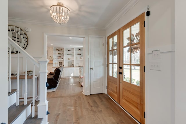 foyer entrance featuring light wood finished floors, a notable chandelier, french doors, and crown molding