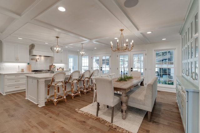 dining area featuring beamed ceiling, a notable chandelier, coffered ceiling, wood finished floors, and french doors