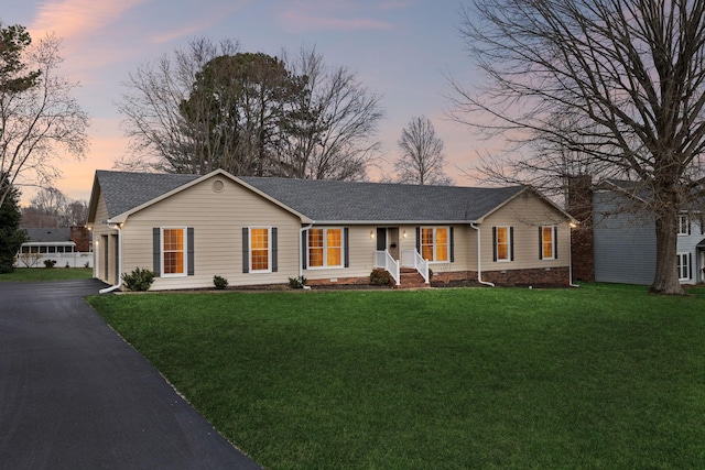 ranch-style house featuring a yard, a garage, driveway, and a shingled roof