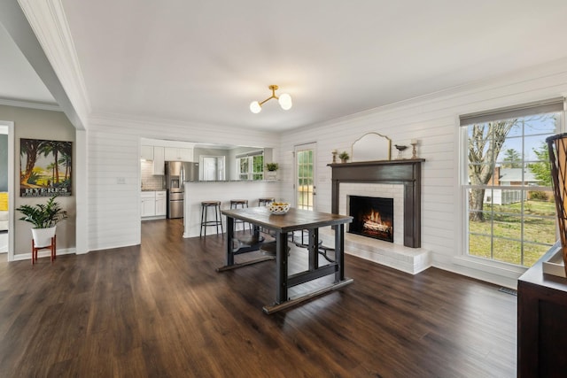 dining area with a wealth of natural light, dark wood-style floors, a fireplace, and ornamental molding