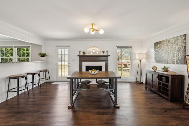 dining area with a fireplace, dark wood-type flooring, an inviting chandelier, and ornamental molding