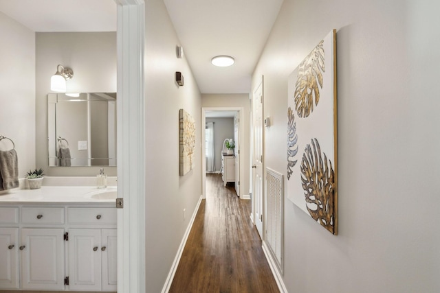 hall with a sink, visible vents, baseboards, and dark wood-style flooring