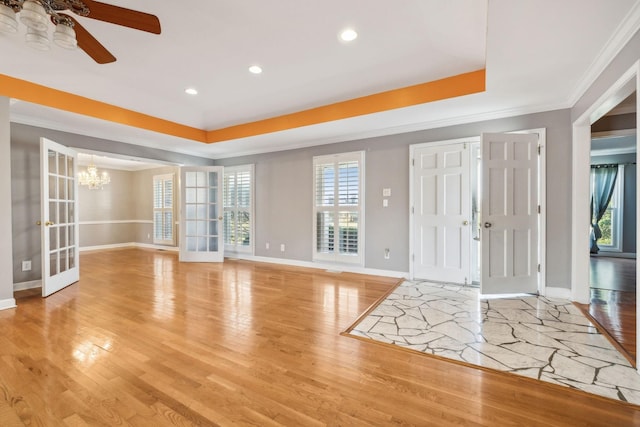 interior space with light wood finished floors, crown molding, baseboards, a tray ceiling, and ceiling fan with notable chandelier