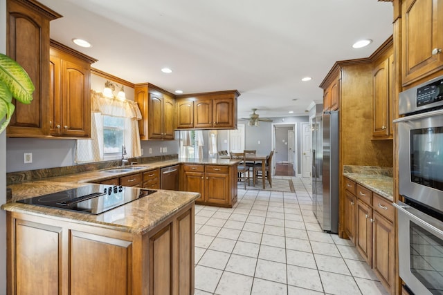 kitchen with a peninsula, ceiling fan, stainless steel appliances, a sink, and brown cabinets