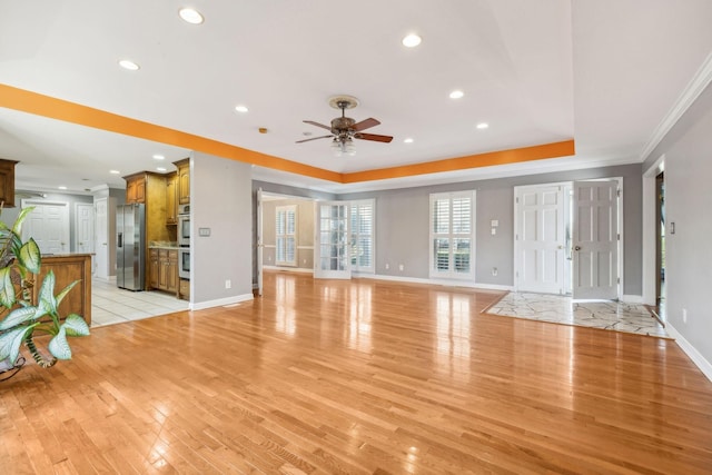 unfurnished living room featuring a tray ceiling, light wood-type flooring, baseboards, and a ceiling fan