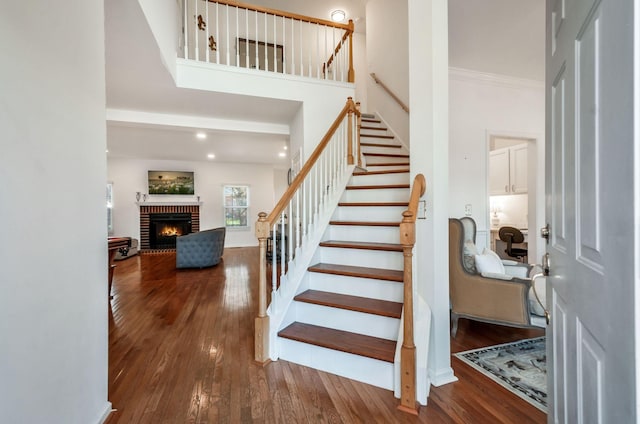 stairs with a high ceiling, wood finished floors, a fireplace, and crown molding