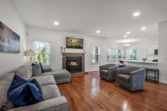 living room with a wealth of natural light, a notable chandelier, a brick fireplace, and dark wood-style flooring