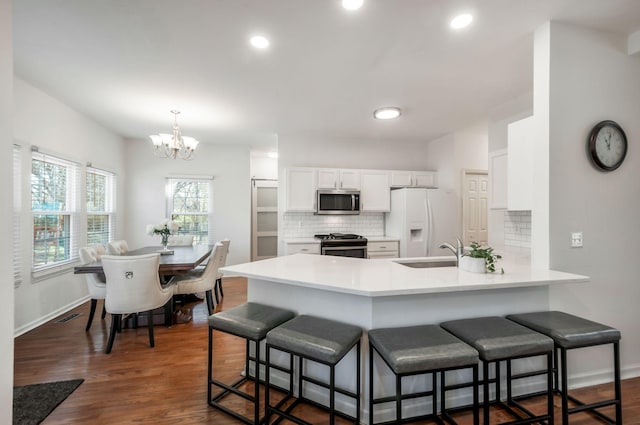 kitchen with appliances with stainless steel finishes, a peninsula, an inviting chandelier, white cabinetry, and a sink