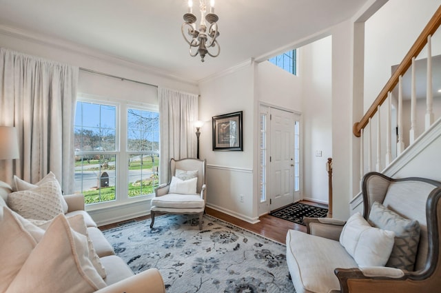 living room with ornamental molding, wood finished floors, an inviting chandelier, baseboards, and stairs