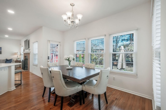 dining space with a notable chandelier, a brick fireplace, baseboards, and wood finished floors