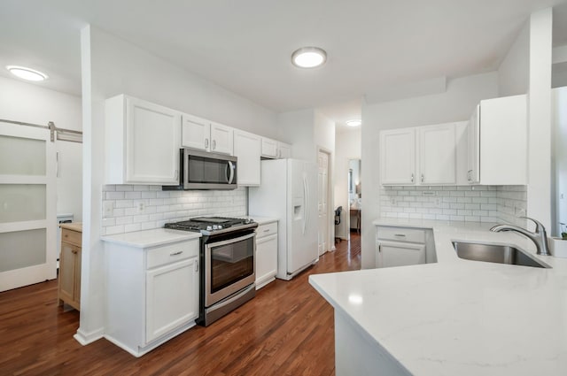 kitchen featuring dark wood-style floors, a sink, decorative backsplash, white cabinets, and appliances with stainless steel finishes