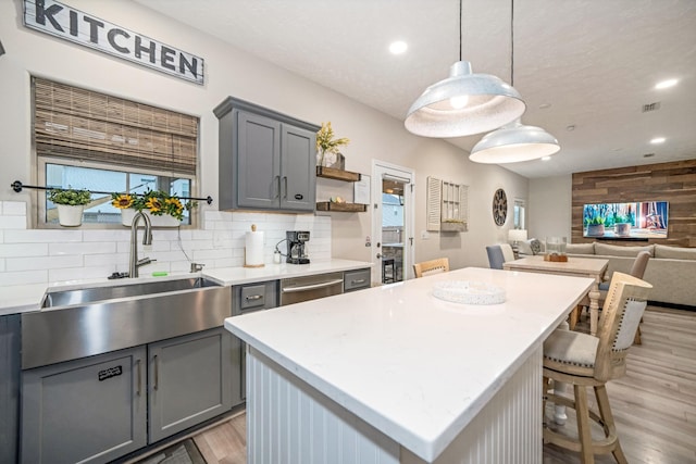 kitchen with gray cabinets, a sink, light countertops, light wood-style floors, and backsplash