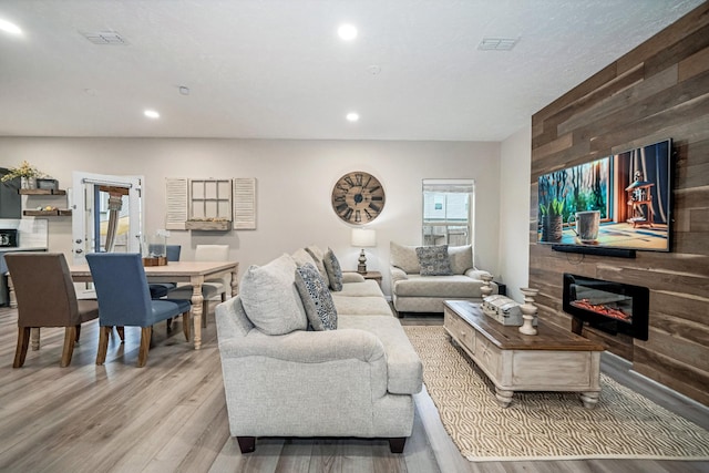 living room with visible vents, a glass covered fireplace, recessed lighting, light wood-style floors, and wooden walls