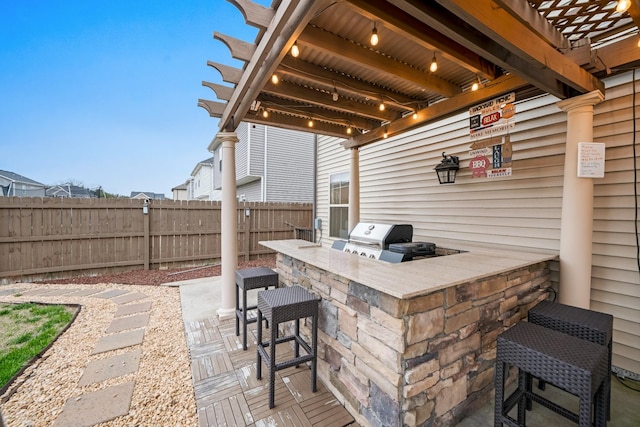 view of patio / terrace featuring outdoor dry bar, fence, an outdoor kitchen, a grill, and a pergola