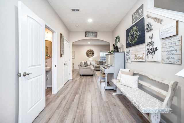 hallway with visible vents, a textured ceiling, wood finished floors, arched walkways, and baseboards