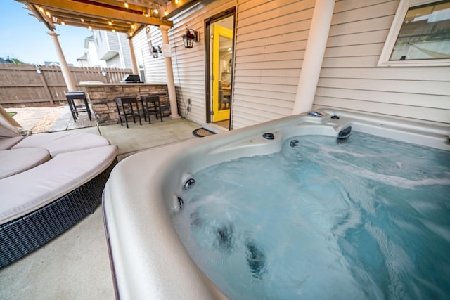 view of patio / terrace with outdoor dry bar, fence, a hot tub, and an outdoor kitchen