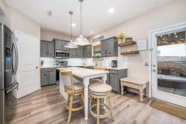 kitchen featuring light wood-style flooring, gray cabinetry, appliances with stainless steel finishes, tasteful backsplash, and a center island