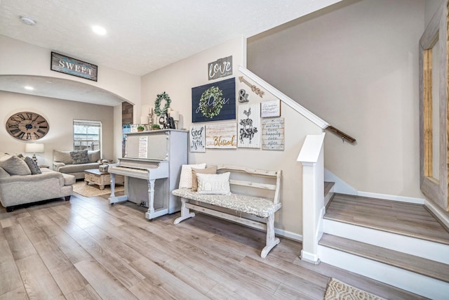 living area with arched walkways, stairs, baseboards, and wood finished floors