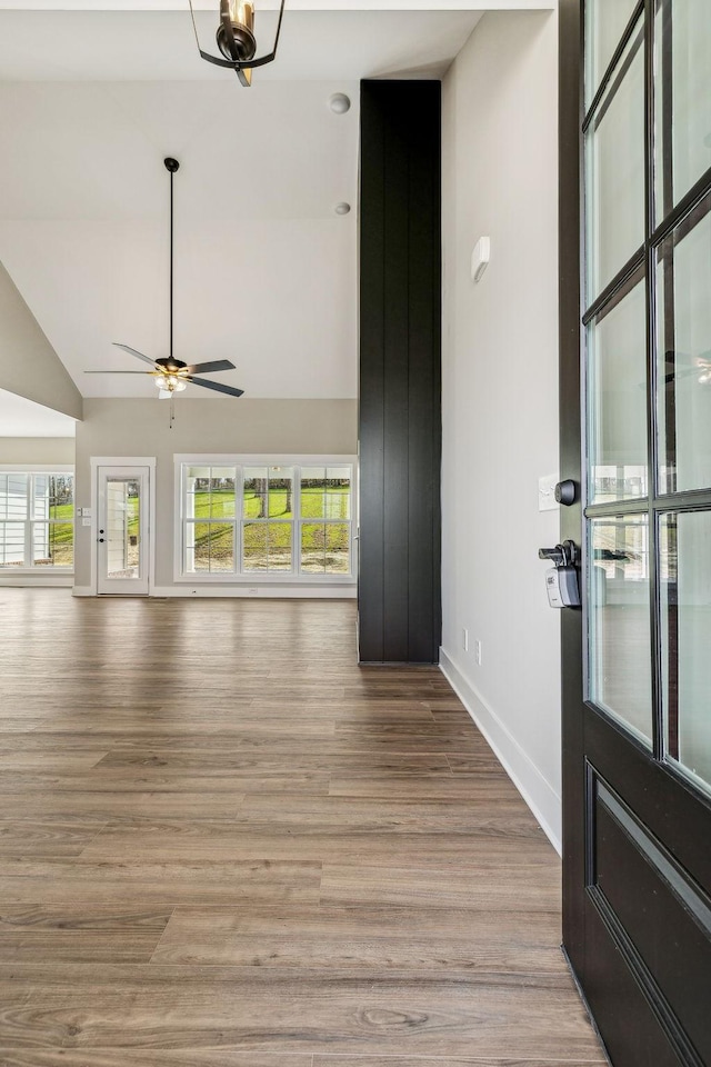 unfurnished living room with a wealth of natural light, baseboards, wood finished floors, and a ceiling fan