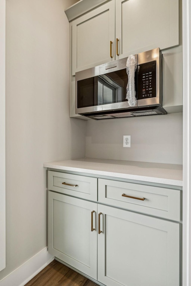 interior space featuring stainless steel microwave, baseboards, dark wood-style flooring, and light countertops