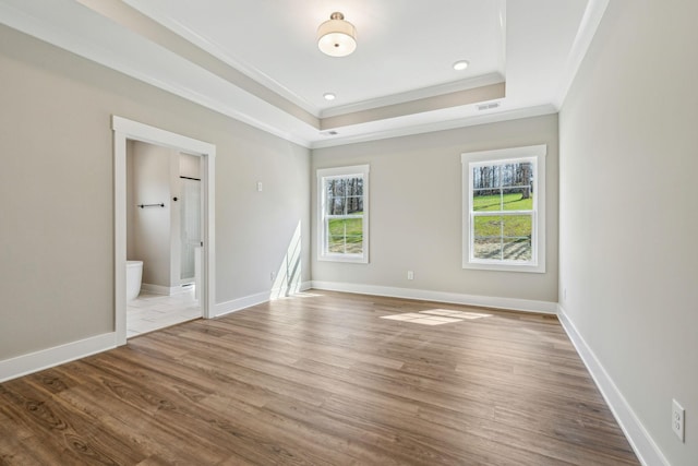 unfurnished bedroom featuring wood finished floors, baseboards, visible vents, ornamental molding, and a raised ceiling