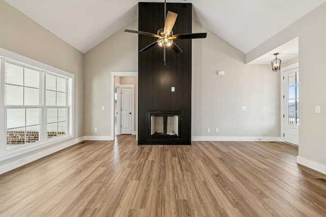 unfurnished living room featuring ceiling fan with notable chandelier, wood finished floors, baseboards, and high vaulted ceiling