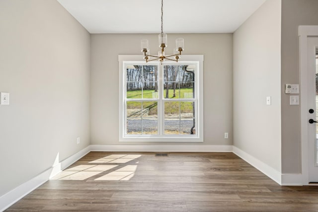 unfurnished dining area featuring visible vents, baseboards, an inviting chandelier, and wood finished floors