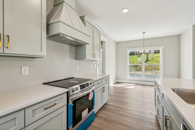 kitchen with light countertops, custom range hood, stainless steel electric range, light wood-style floors, and a notable chandelier